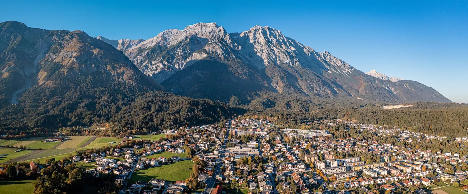 Alpine town nestled below rugged, forested mountains under a clear blue sky
