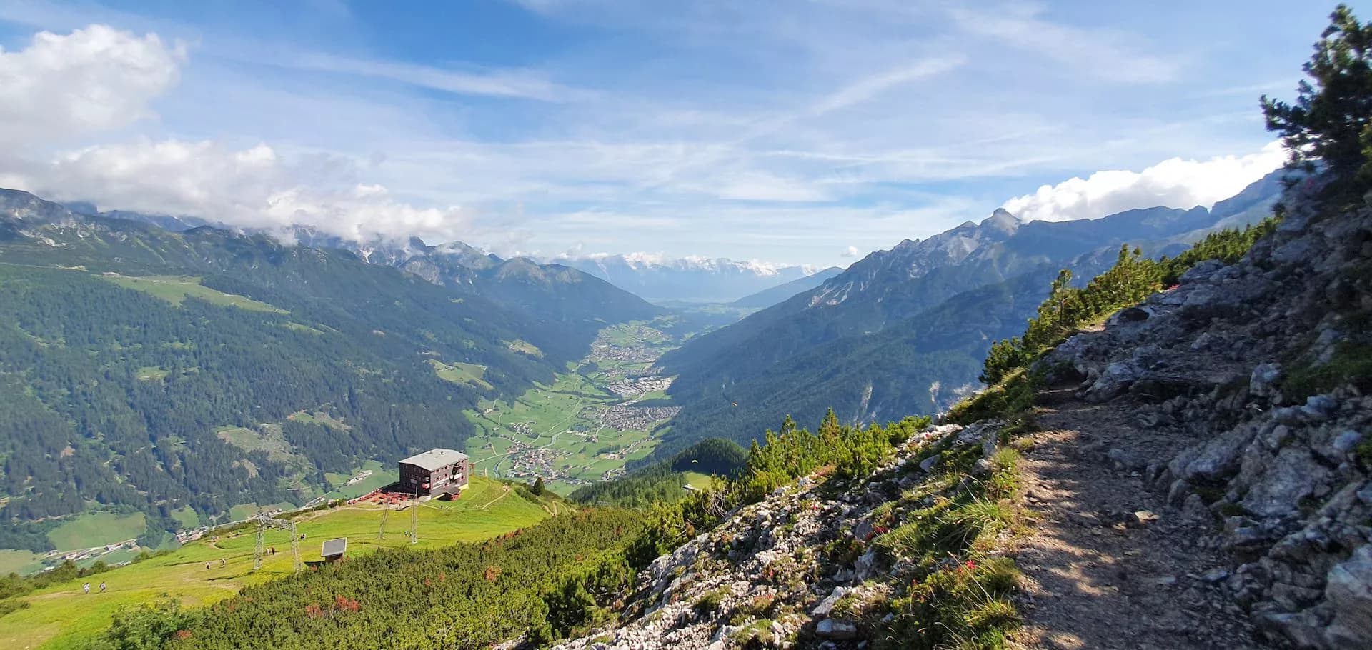 Hiking trail above Elferhütte overlooking Stubai Valley with green mountains and distant snow peaks.